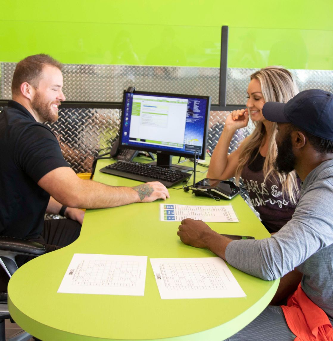 10GYM Jenks staff member helping two new members review the Preferred and Basic membership options at the front desk during a signup consultation.