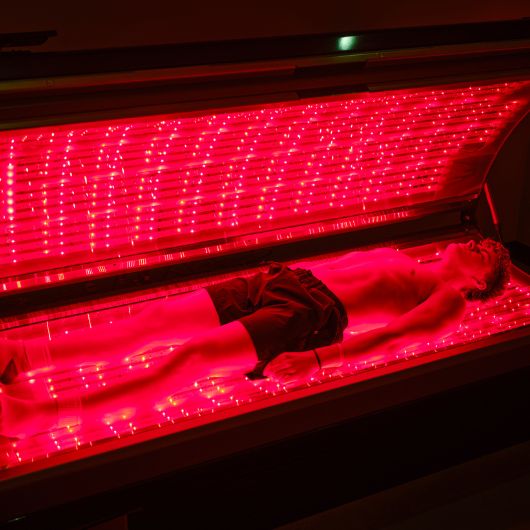 Member using a full-body red light therapy bed to support muscle recovery and circulation at 10GYM Jenks