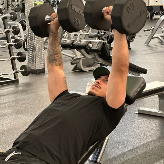Man performing an incline dumbbell press in the strength training area at 10GYM Jenks