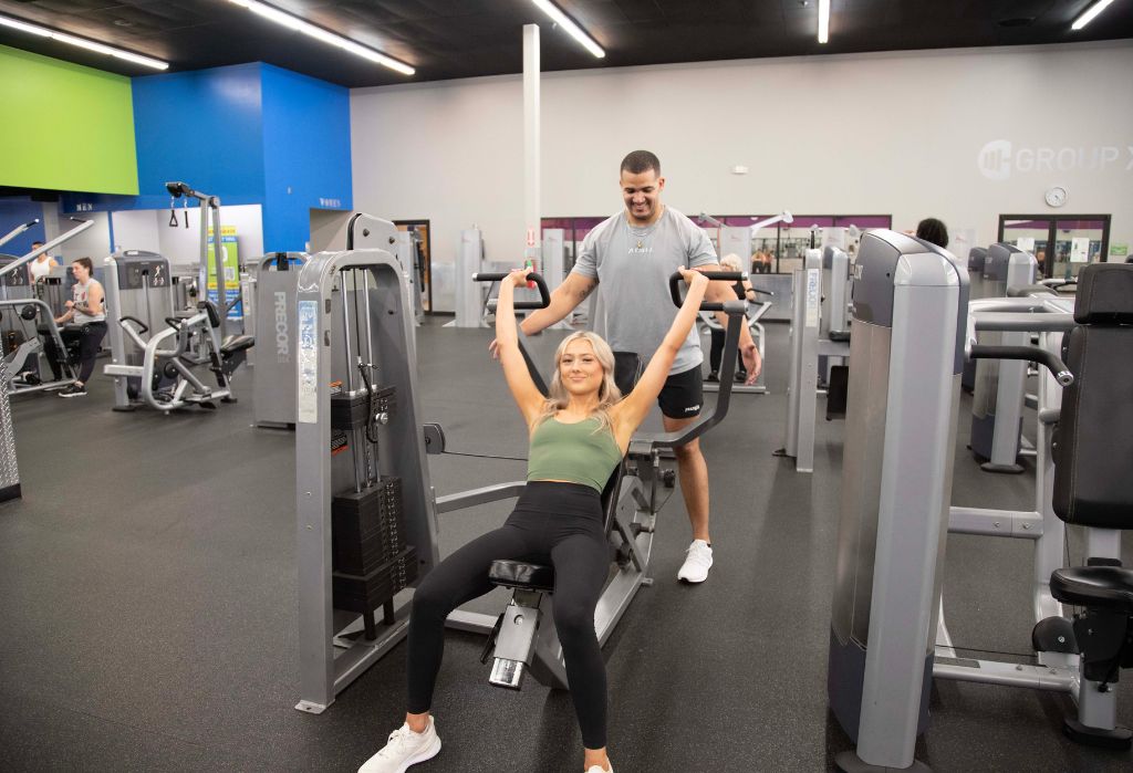 Member using strength training machines with trainer support at 10GYM Jenks fitness center.