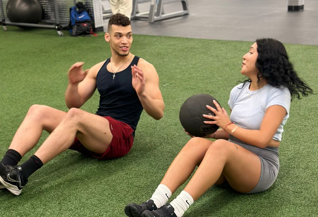 Two 10GYM Jenks members doing a partner medicine-ball workout on the functional turf area, showcasing the welcoming and energetic gym environment.