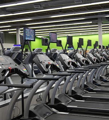 rows of cardio equipment and a gym members using a treadmill