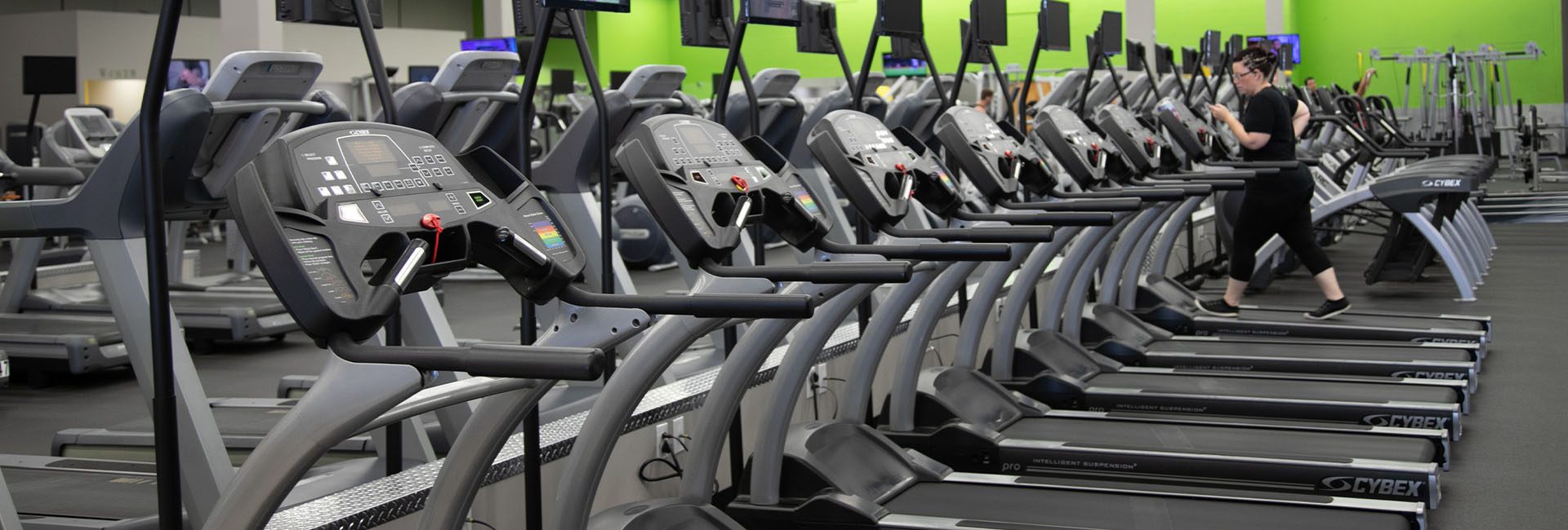 rows of cardio equipment and a gym members using a treadmill