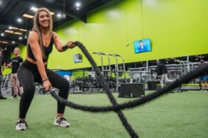 Woman performing battle rope exercises in a gym with green walls and turf flooring at 10GYM.