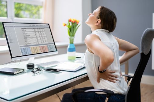 Woman stretching her back after sitting at a desk during the workday.